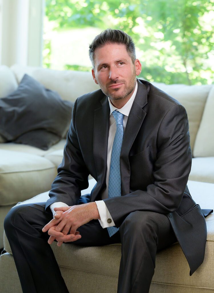 Man sitting on ottoman in suit, looking off to the side