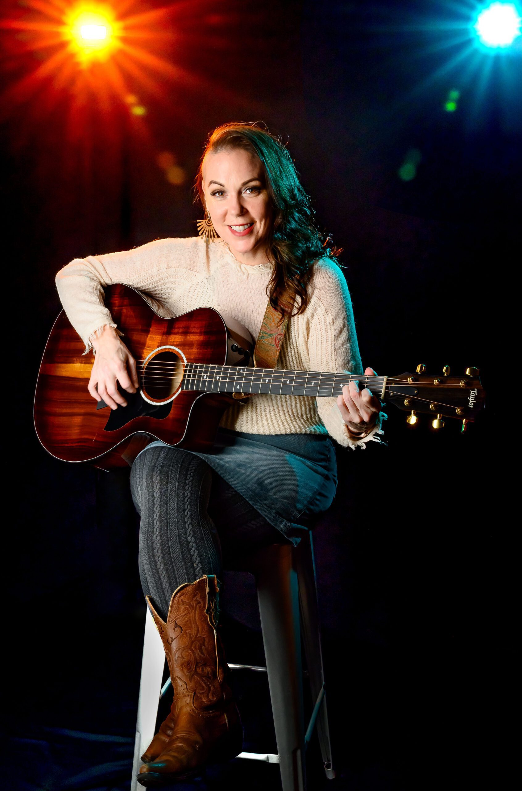 Woman sitting on a stool holding a guitar with colorful lights behind her