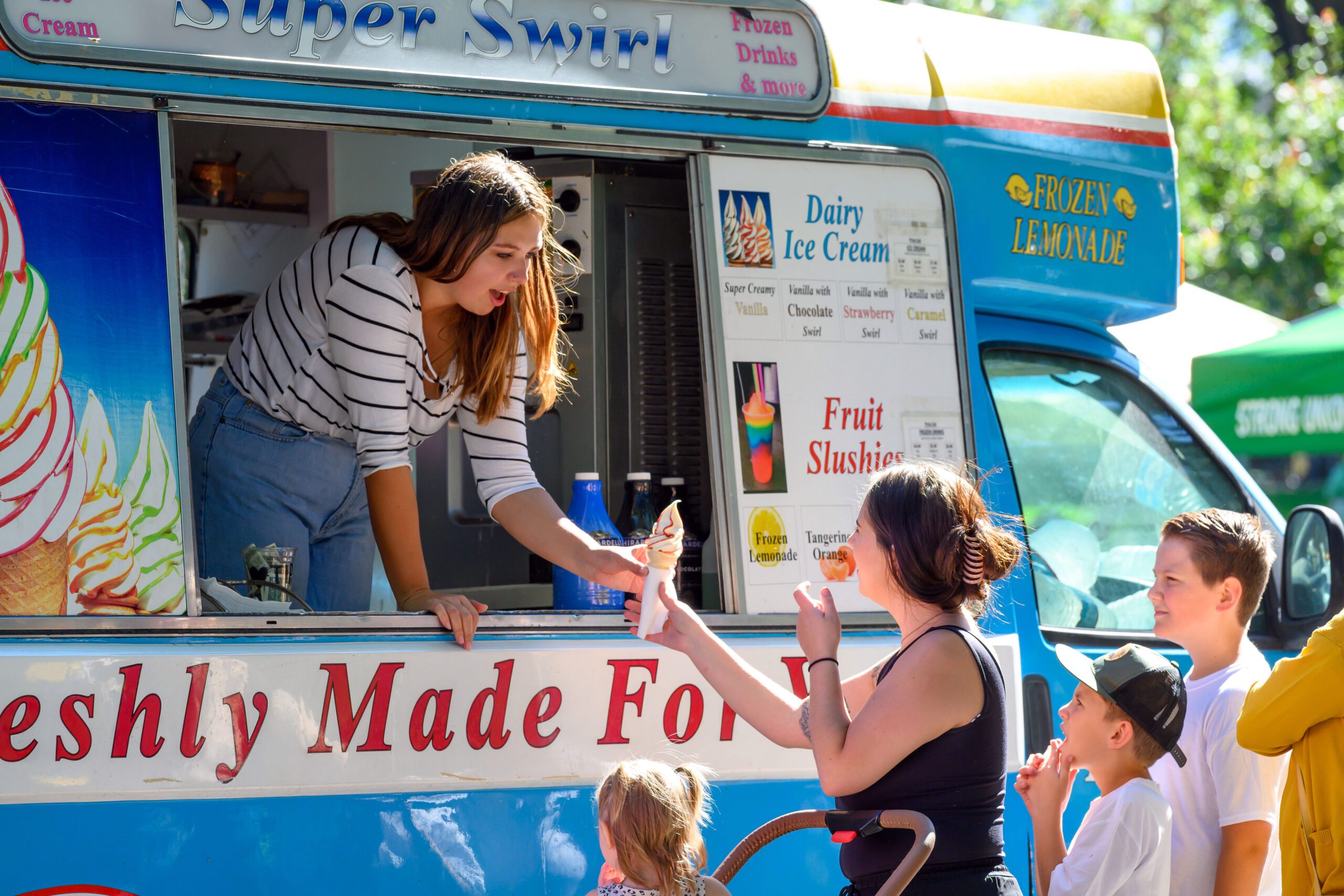 Woman in ice cream truck hands ice cream to people