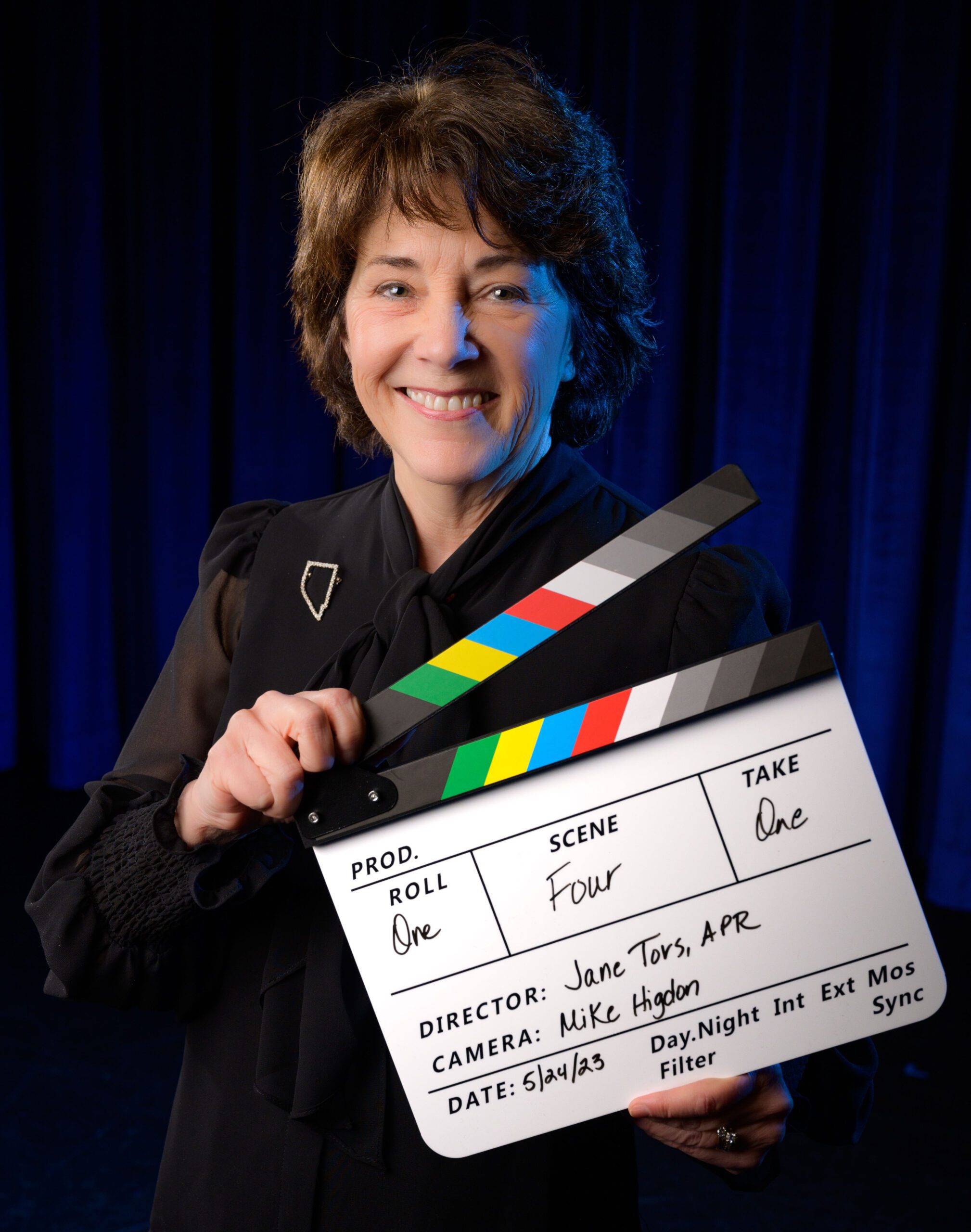 Woman holds movie clapper in front of blue curtains