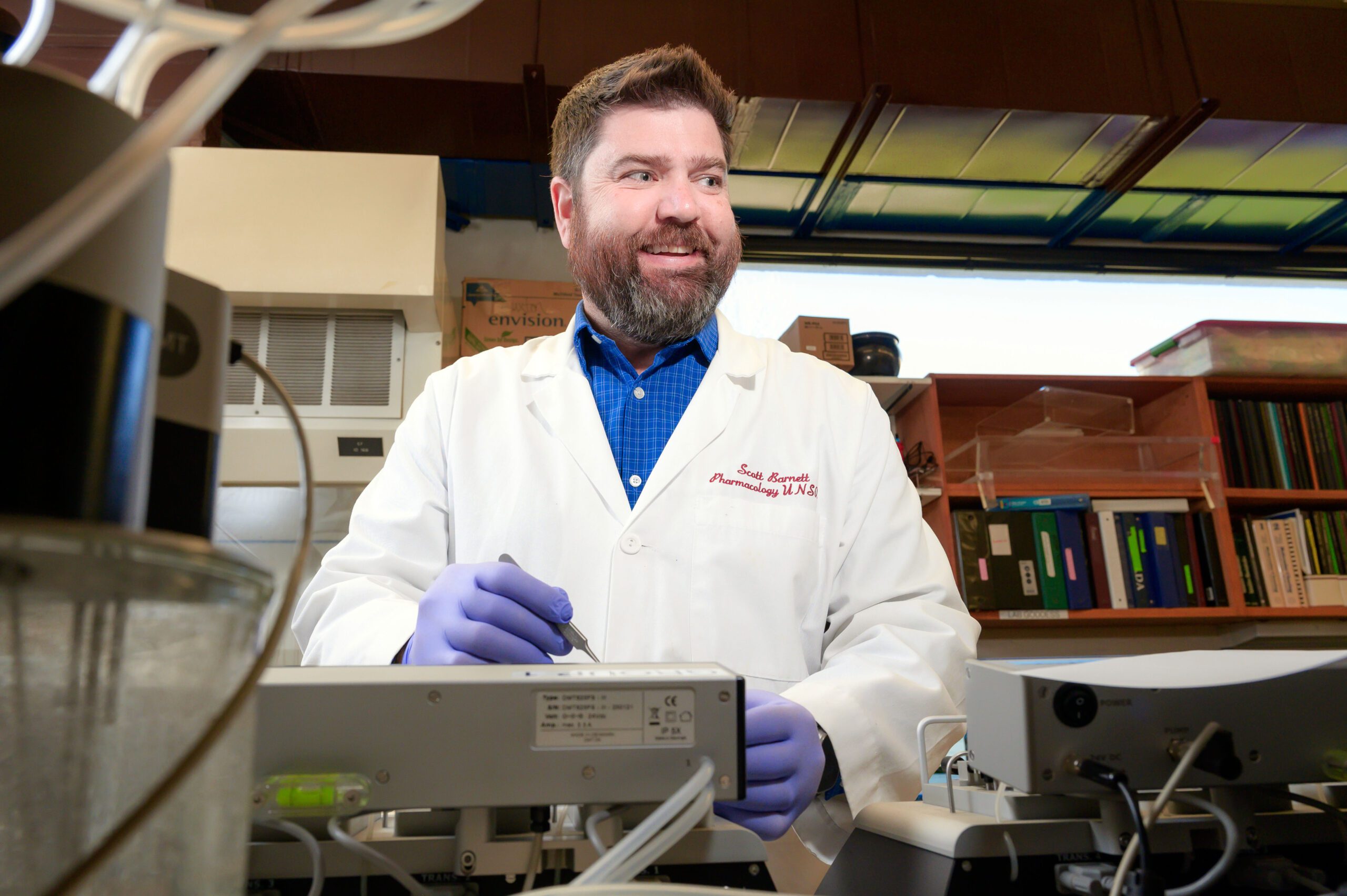 Scientist works with equipment, looks off to right and smiling.