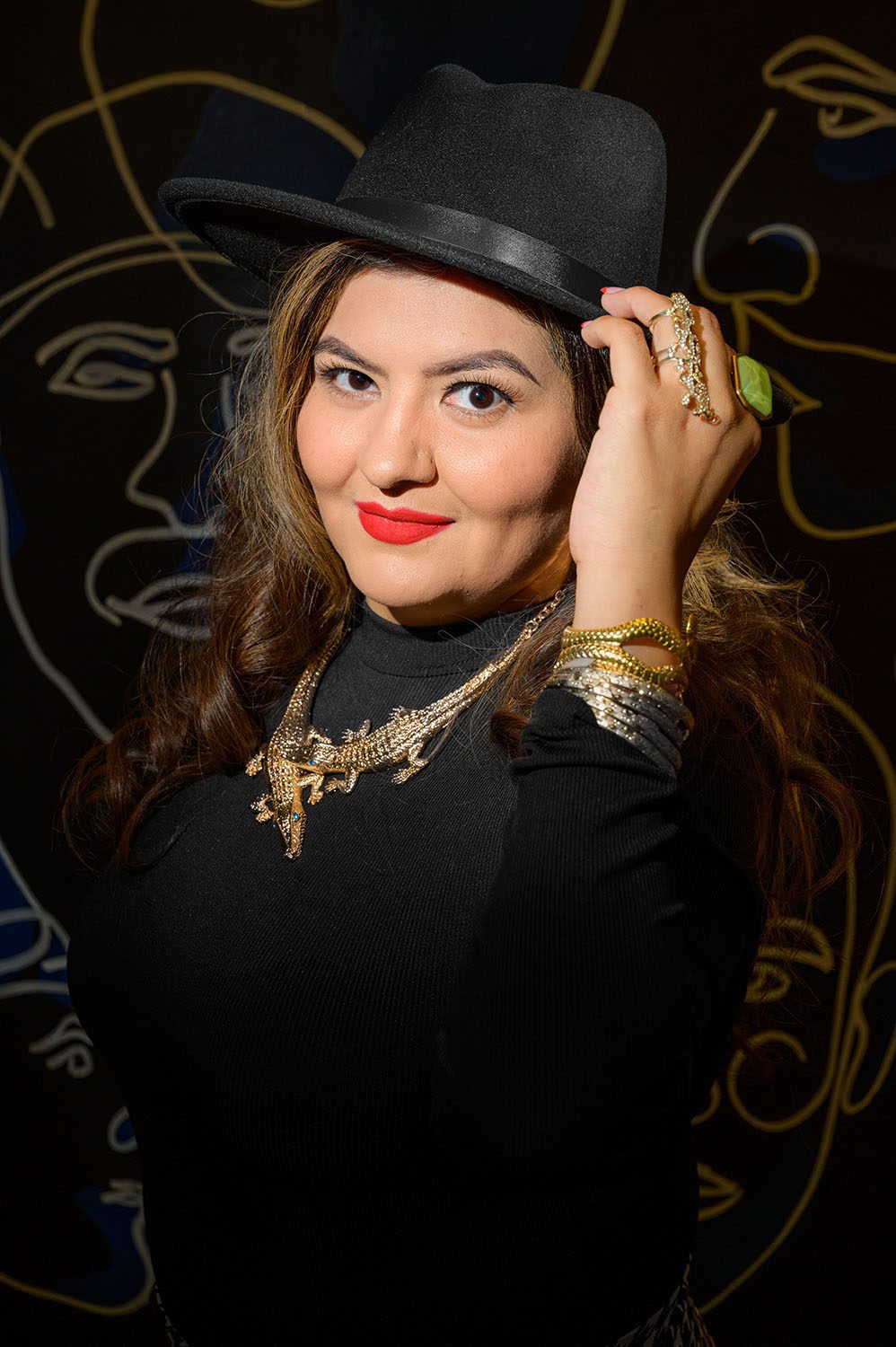 Professional photography of Woman stands in front of mural while wearing large hat and alligator jewelry